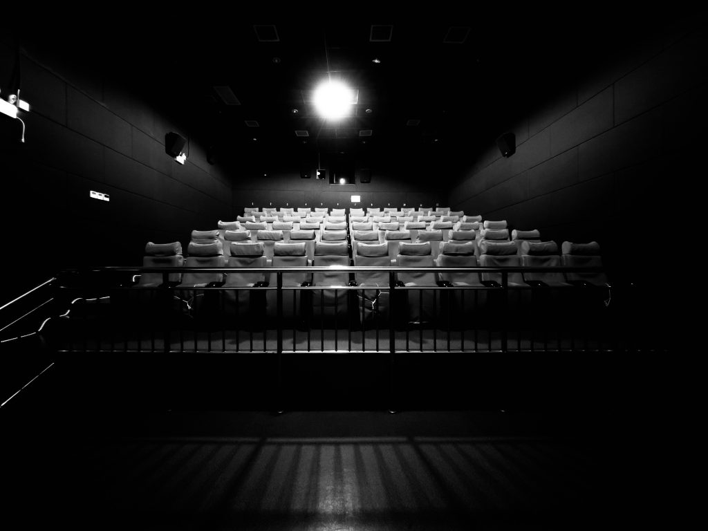 Moderne Kinobestuhlung mit leeren Sitzen und Blick auf die Leinwand, schwarz-weiß Aufnahme.